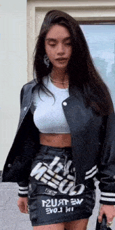 a woman wearing a black leather jacket and a white crop top .