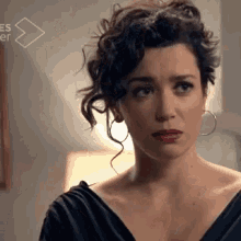 a woman with curly hair is wearing hoop earrings and a black dress