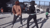two women are dancing in a parking lot in front of a fence