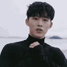 a young man wearing a black turtleneck is standing in front of the ocean .