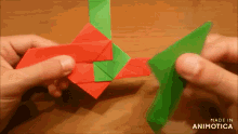 a person is holding a red and green origami piece with the words made in animotica below it