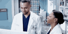 a man and a woman in lab coats are looking at a computer screen in a hospital room .