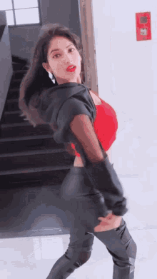 a woman in a red top and black leather pants is standing in front of stairs .