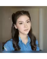 a woman wearing a denim shirt and a braided ponytail looks at the camera