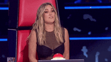 a woman in a black top sits in a chair with a red button that says ' audition ' on it