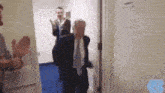 a man in a suit and tie is walking through a doorway while a group of people applaud .