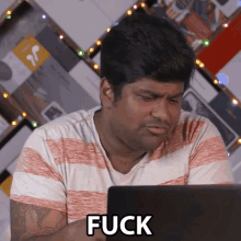 a man is sitting in front of a laptop with the word fuck on the screen