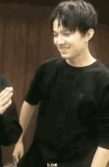 a young man in a black t-shirt is smiling while standing next to another young man .