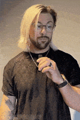 a man with blonde hair and glasses is wearing a black t-shirt and a ring on his finger