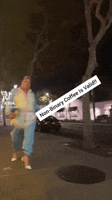 a woman walking down a sidewalk with a sign that says non-binary coffee is valid