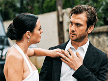 a man and a woman are standing next to each other and the woman is touching the man 's tie