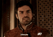 a man with a beard is saying `` i love you '' while wearing a brown jacket .