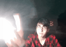 a man wearing glasses and a plaid shirt is holding a light in his hand