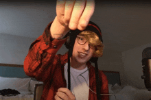 a young man wearing headphones and a red plaid shirt holds up his fingers
