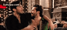 two men are hugging each other in a room with a crowd .