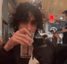 a man drinking from a glass with a red exit sign above him