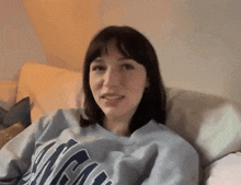 a woman is sitting on a couch wearing a sweatshirt that says ' ncr ' on it .