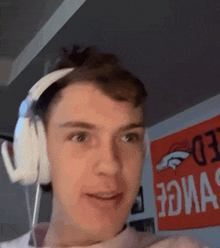 a young man wearing headphones is standing in front of a sign that says denver broncos .
