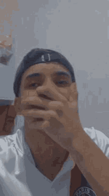 a man wearing a hat is covering his mouth with his hand .