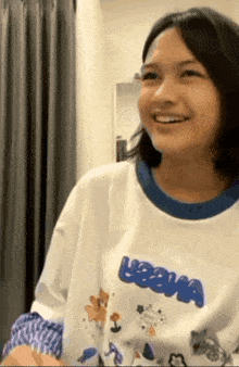 a young girl wearing a white t-shirt with a blue collar is smiling and looking at the camera .