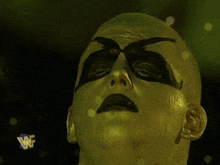 a wrestler with gold paint on his face has a blue w logo on his arm