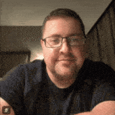 a man wearing glasses and a blue shirt smiles for the camera