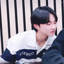 a young man is sitting at a table with his eyes closed and wearing a sweater that says stereo on it .