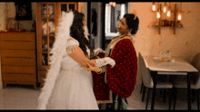 a woman in a white dress with angel wings holds another woman 's hand