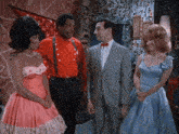a man in a suit stands between two women in pink dresses and a man in a red shirt