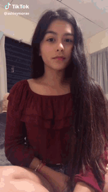 a girl in a red off the shoulder top is sitting on a couch .