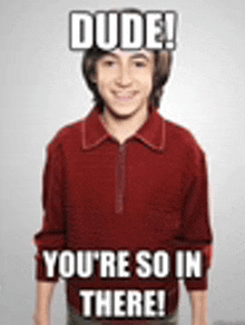 a young man in a red shirt is standing in front of a white background with a meme on his head .