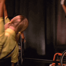 a woman in a yellow shirt is doing a handstand in front of a black curtain