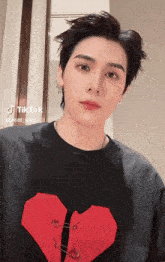 a young man wearing a black shirt with a red heart and safety pins