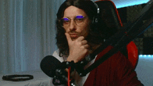 a man wearing glasses and headphones holds his hand to his chin