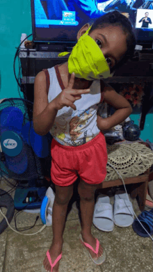 a little girl wearing a yellow mask is standing in front of a fan