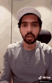 a man with a beard is wearing a white hat and a necklace with tiktok written on the bottom right