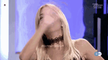 a woman wearing a choker covering her face with her hand on a television screen