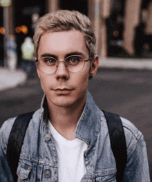 a man wearing glasses and a denim jacket is looking at the camera