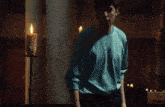 a man in a blue shirt sits in a dark room with candles in the background