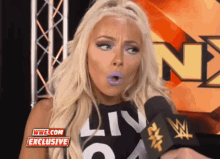 a woman with purple lips is talking into a microphone with a wwe.com exclusive sign above her