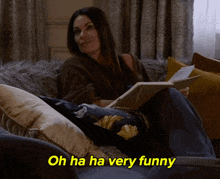 a woman is sitting on a couch reading a book and the words oh ha ha very funny are next to her