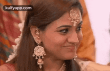 a woman wearing earrings and a maang tikka on her forehead is smiling .