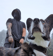 a man in a black hoodie stands next to a black and white dog on a leash