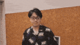 a man wearing glasses and a hawaiian shirt is standing in front of a wall .