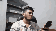 a man with a beard is sitting in a chair holding a cell phone in his hand .