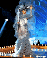 a woman in a white dress with ruffles and a hat is on a stage