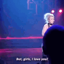 a woman singing on stage with the words but girls i love you behind her
