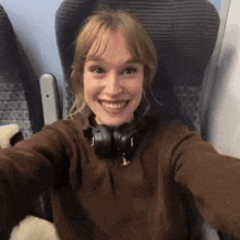 a woman wearing headphones smiles while taking a selfie on a plane