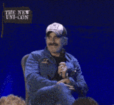 a man sitting in front of a sign that says the new uni con