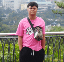 a man wearing a pink shirt that says hi on it stands in front of a railing